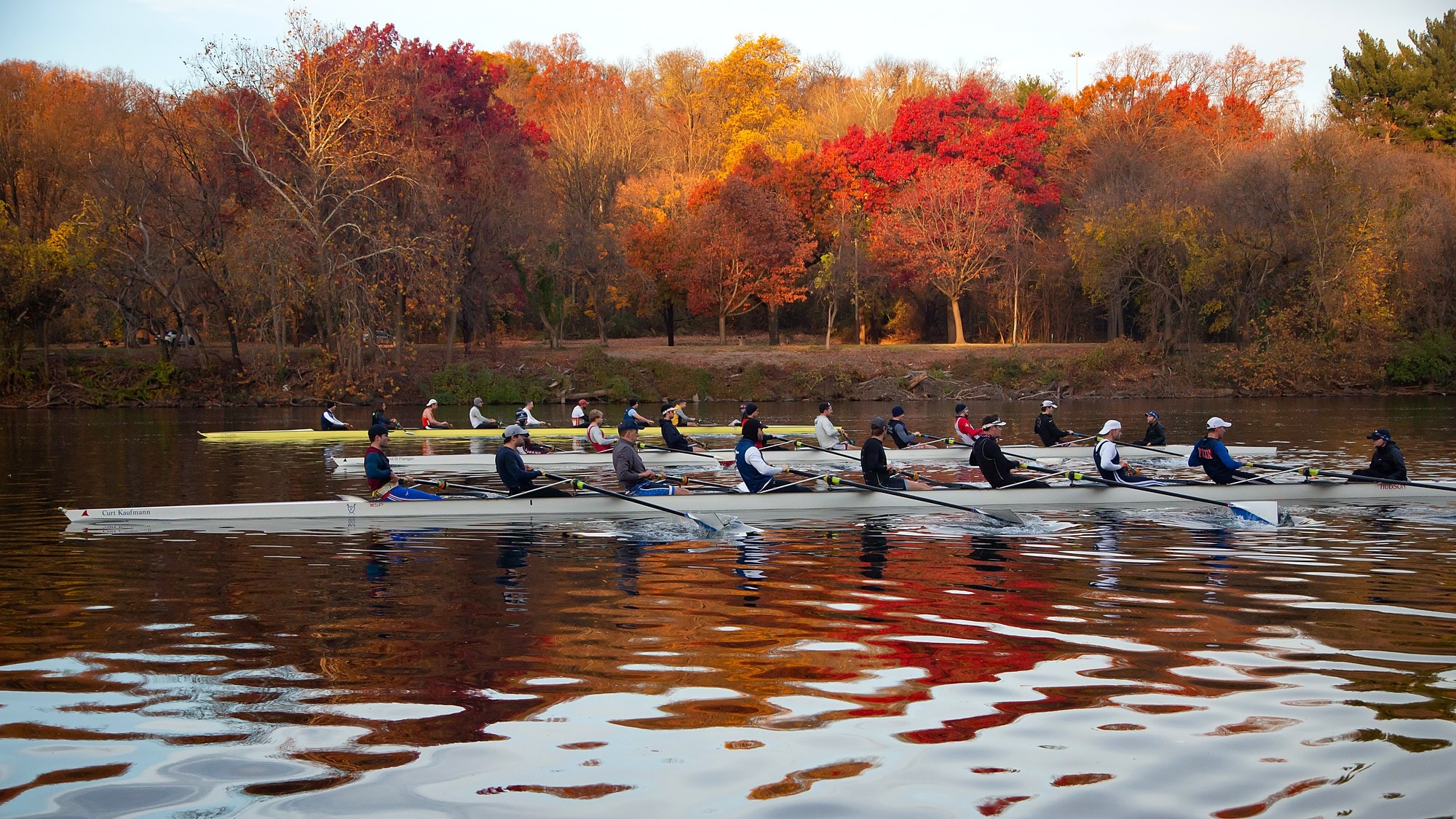 A Fairmount eight rowing past bright red and orange fall trees